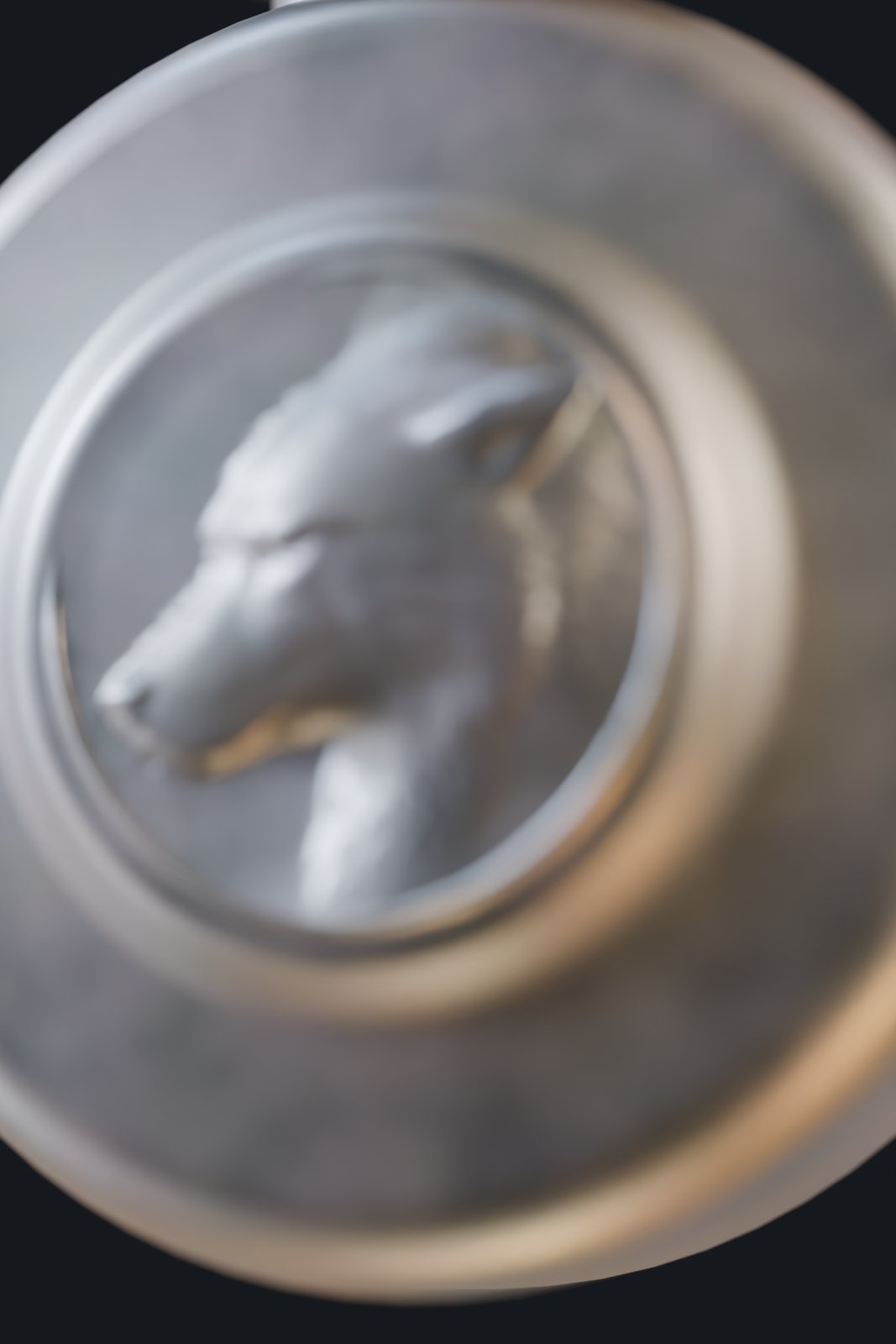 The wheel pommel with a direwolf head in low relief, lit from the side so the relief reads.